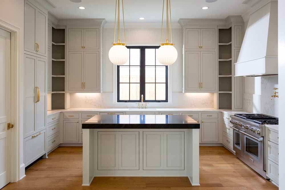 Modern kitchen with light gray cabinets, a black-topped island, two globe pendant lights, and stainless steel appliances.