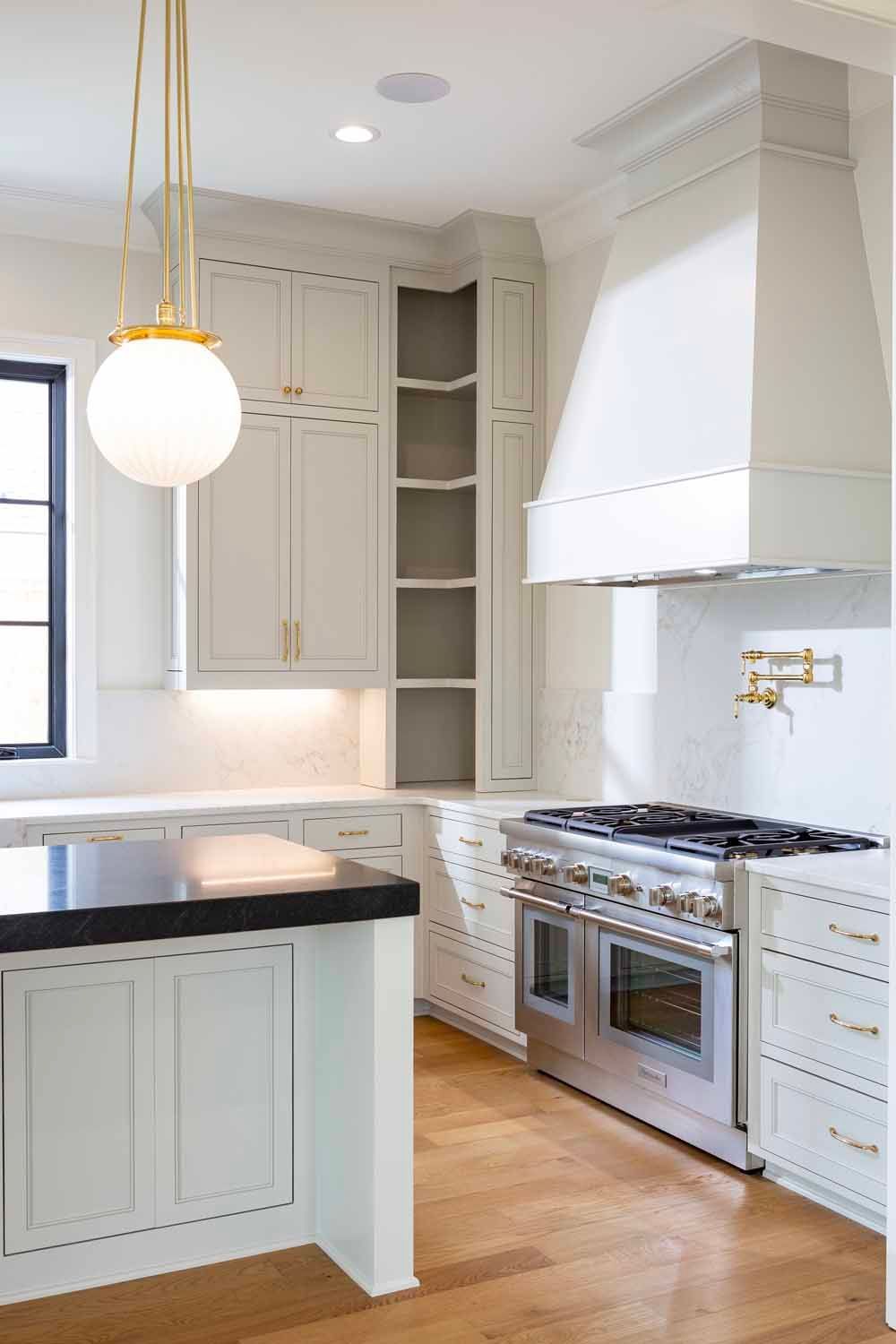 A bright kitchen with light-gray cabinetry, a large white range hood, stainless steel stove, and a spherical pendant light.