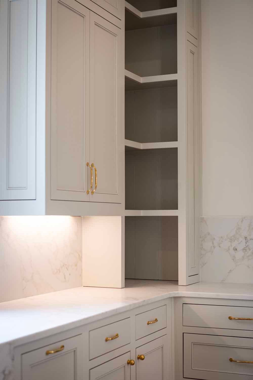 White kitchen cabinetry with open corner shelving, marble countertops, and gold-toned hardware.