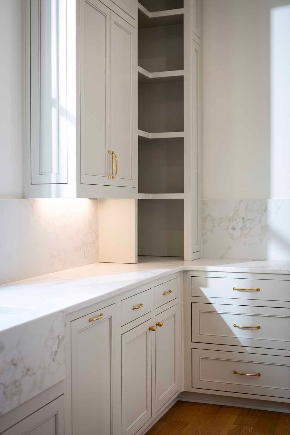 White kitchen cabinets with brass hardware, a marble countertop, and open shelving in the corner.