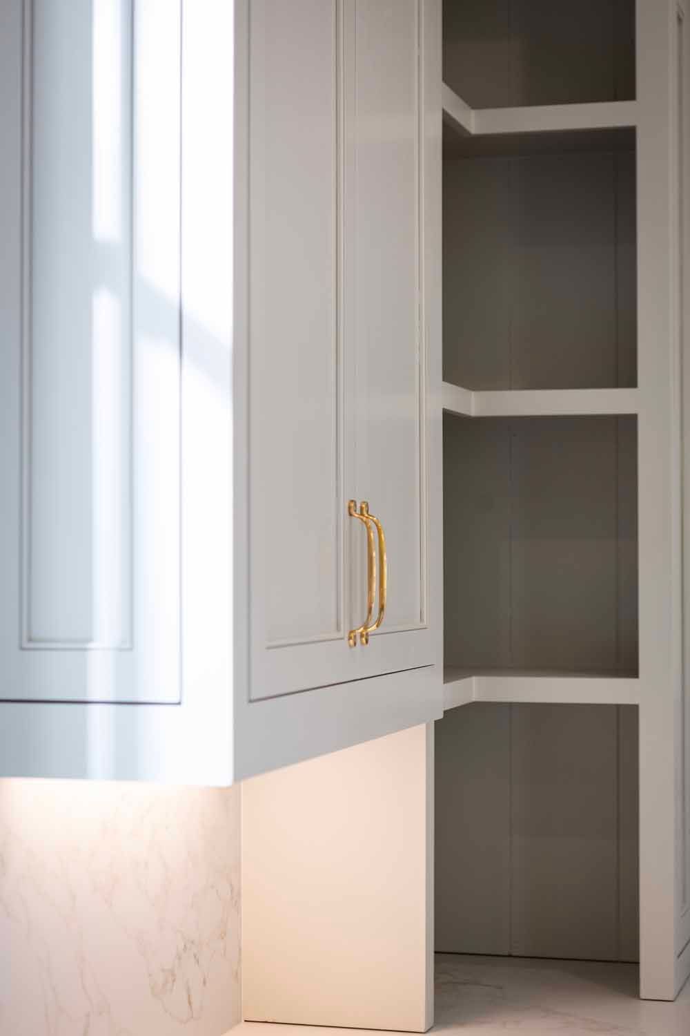 White kitchen cabinets with gold handles beside open corner shelving with under-cabinet lighting.