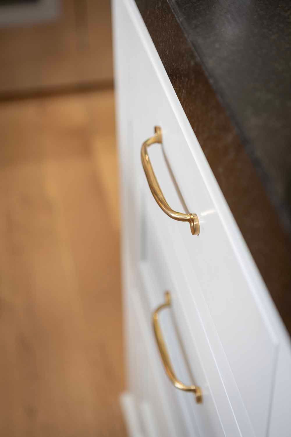 White kitchen cabinets with brass handles and a dark countertop, viewed from a slightly high, angled perspective.