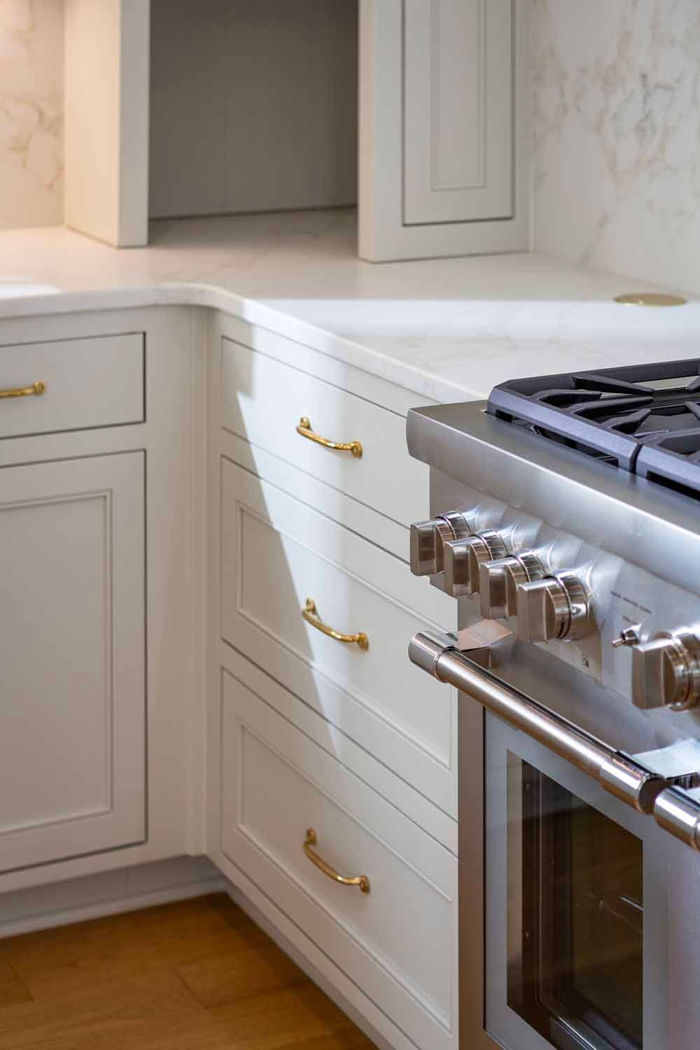 A close-up of a kitchen corner with white cabinets, gold hardware, and a stainless steel range stove.