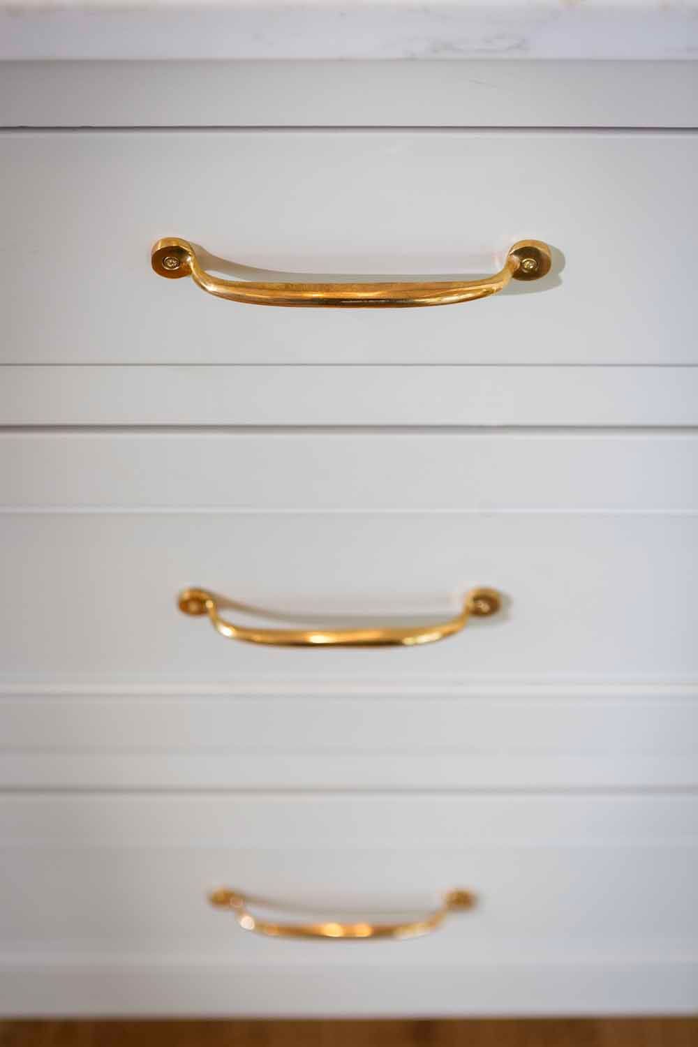 Three white drawers stacked vertically, each featuring a sleek, horizontal polished gold handle.