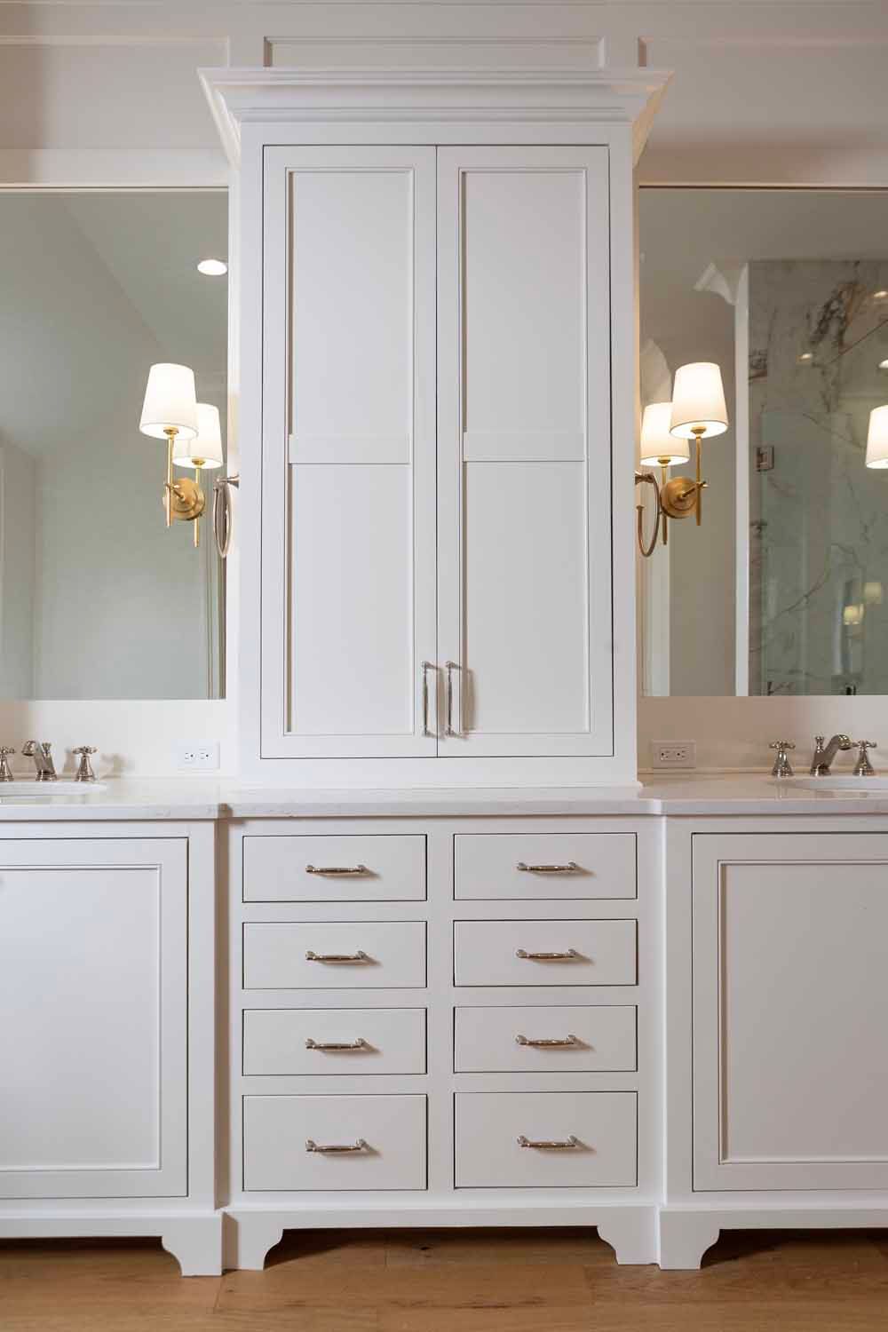 A symmetrical white bathroom vanity with two sinks, a central tower cabinet, and eight storage drawers with silver handles.