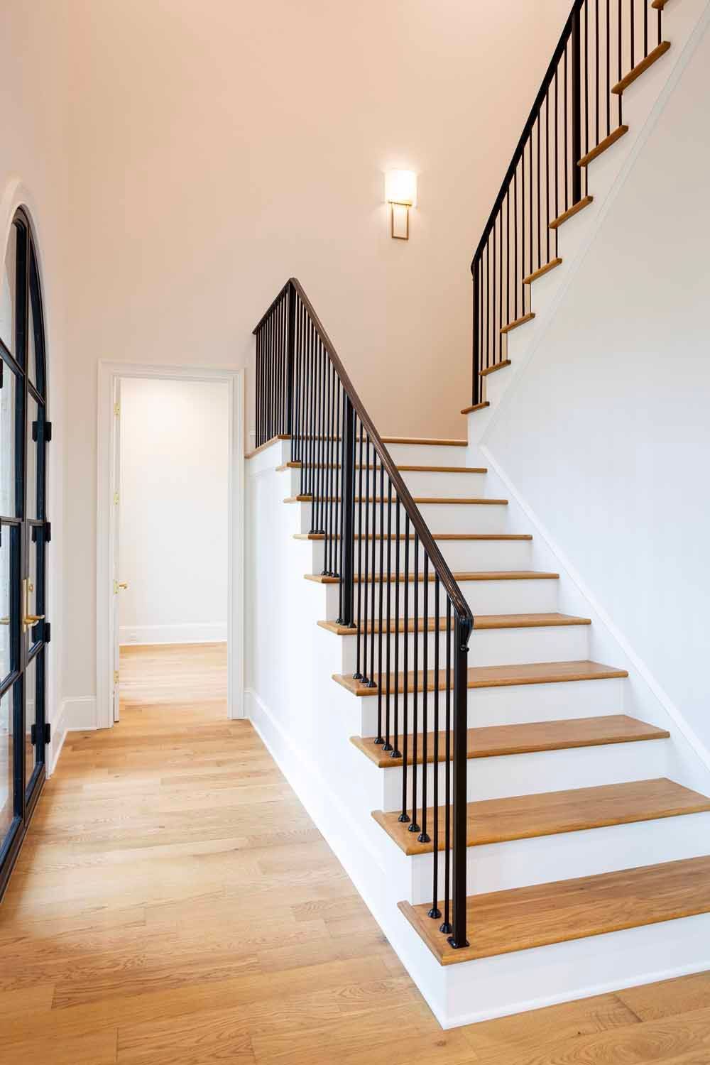 A bright entryway with a staircase featuring wooden treads, white risers, and thin black metal railings on light wood floors.