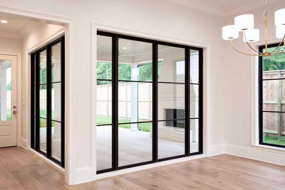 A modern, bright room featuring black-framed floor-to-ceiling glass patio doors opening to an outdoor living space.