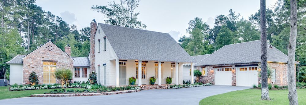A two-story white house with brick accents, a gray shingled roof, a covered front porch, and an attached two-car garage.