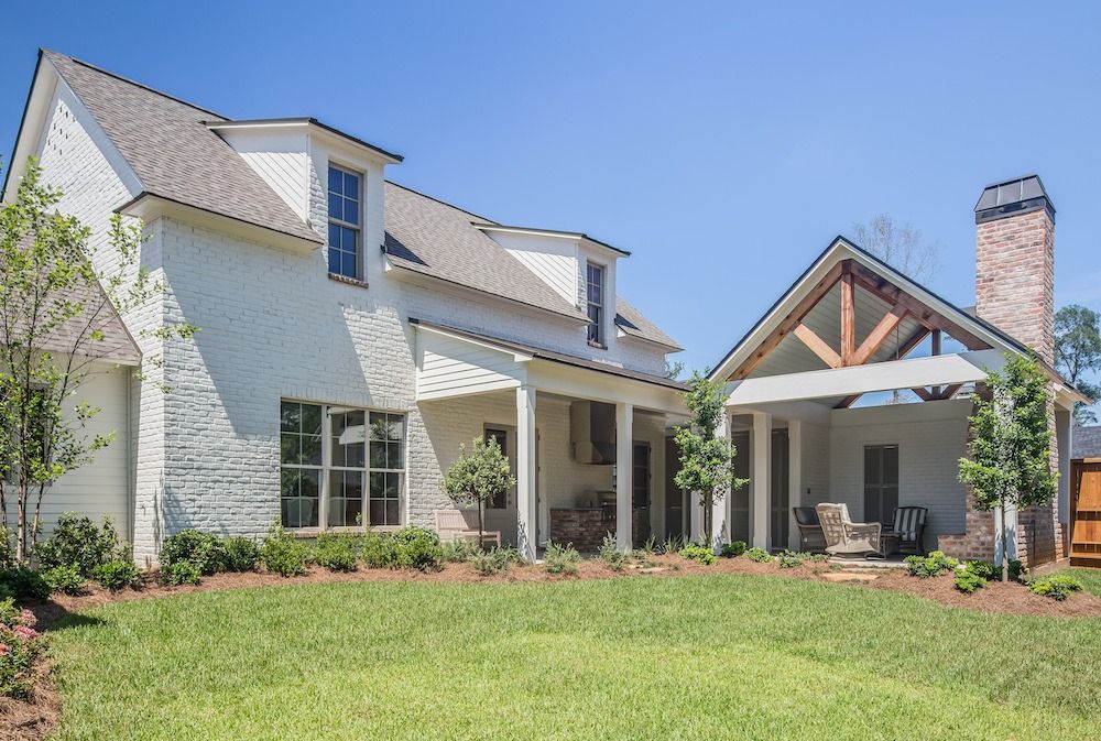 A modern two-story white brick house with a steep roof, dormer windows, and an outdoor covered patio with a brick chimney.