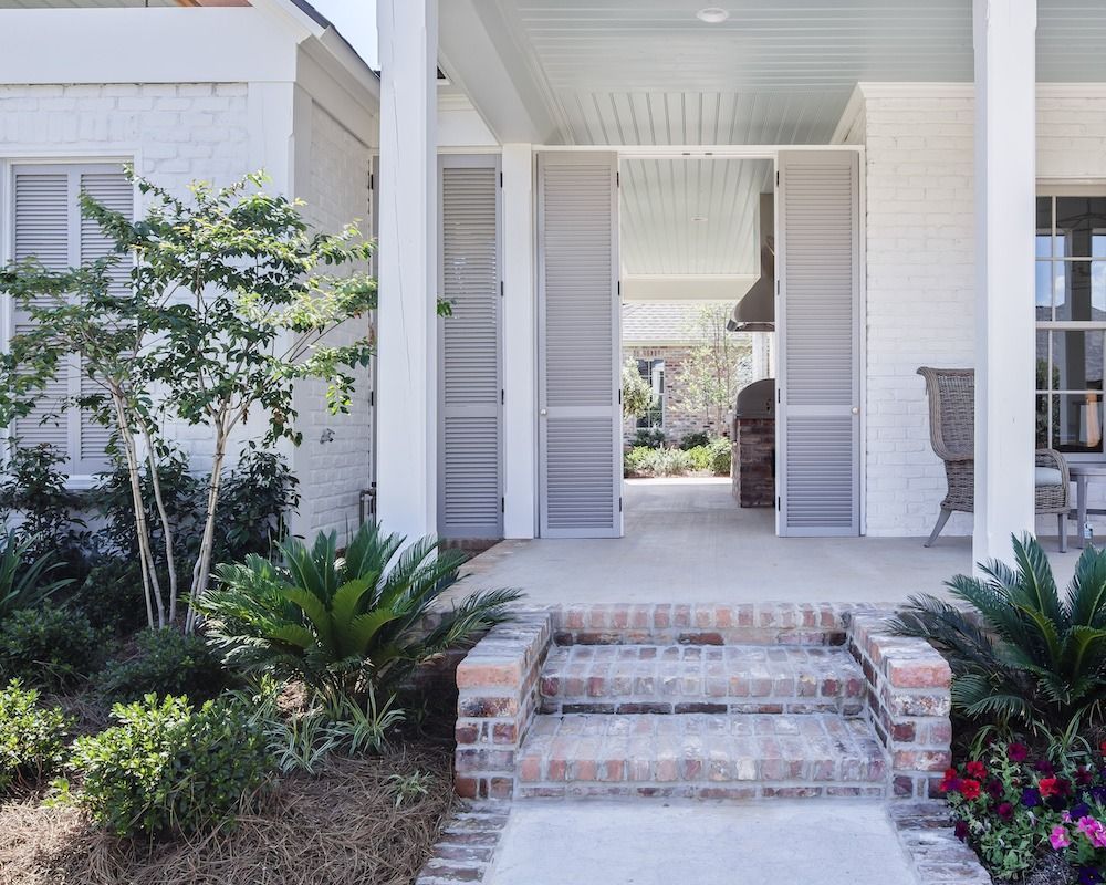 White brick home exterior with a covered porch, brick steps, and screen doors leading to a backyard patio area.