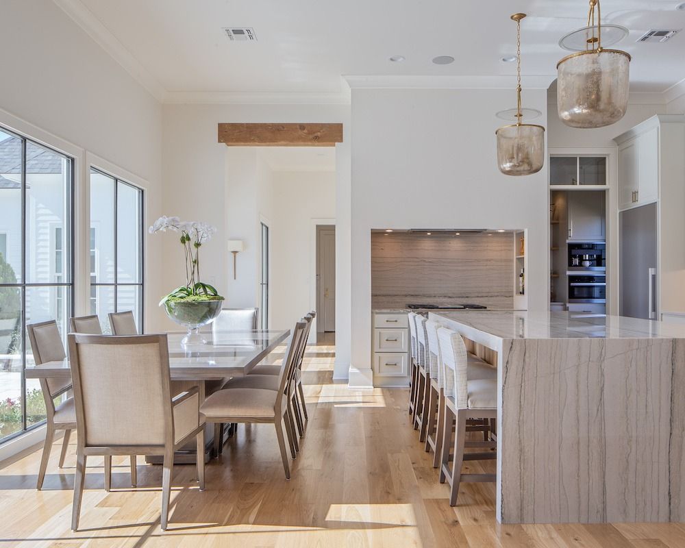 Bright, open-concept dining room and kitchen with a long stone island, light wood floors, and modern, neutral furniture.
