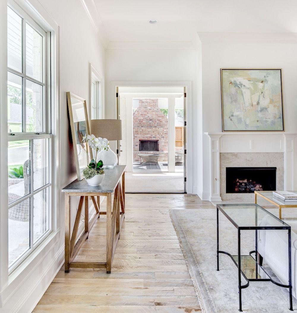 A bright hallway with light wood floors leading to an outdoor fireplace, featuring a console table and a wall fireplace.