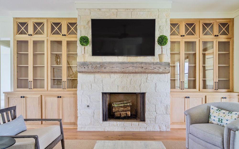A fireplace with a stone facade, rustic wooden mantel, and TV, flanked by light wood cabinetry and two armchairs.