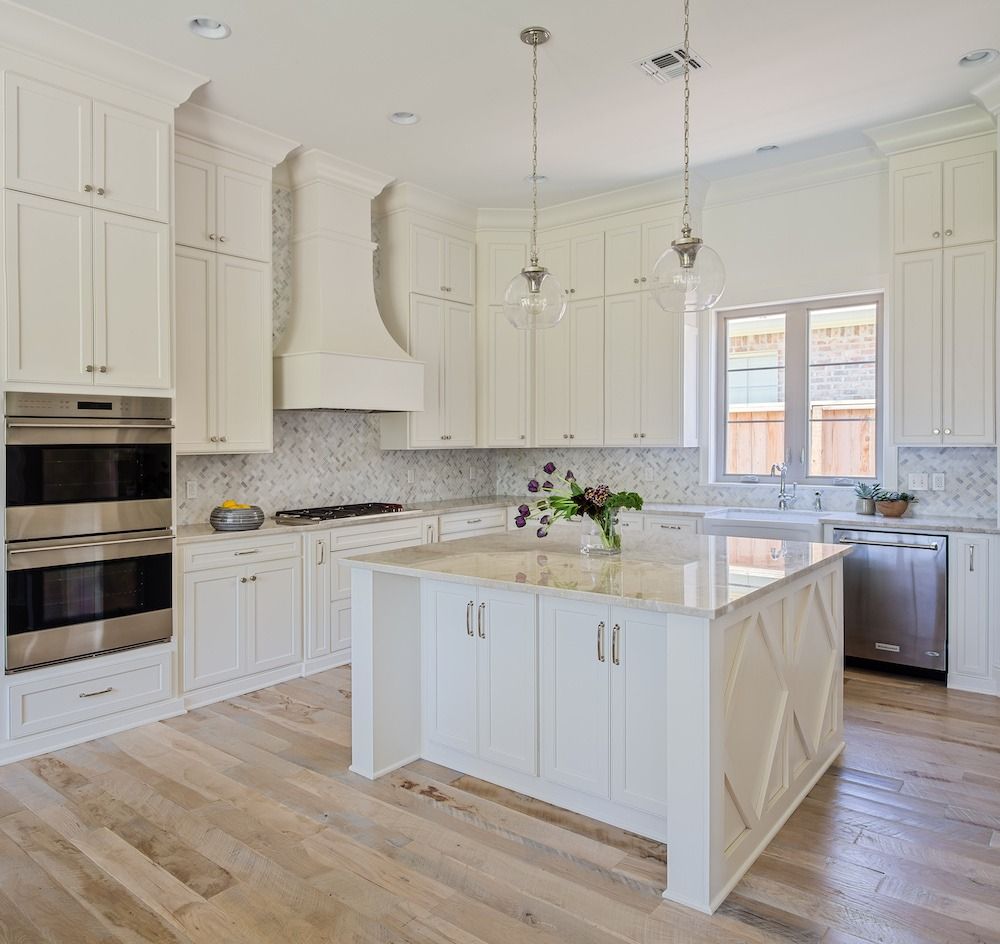A bright kitchen with cream cabinets, a large central island, stainless steel appliances, and light wood flooring.