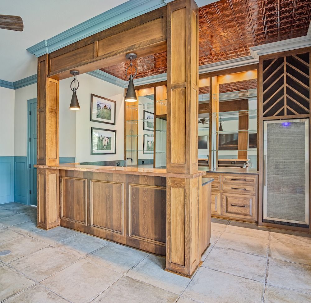 A home bar with wood cabinetry, a copper-tiled ceiling, two pendant lights, and a glass-door wine refrigerator.