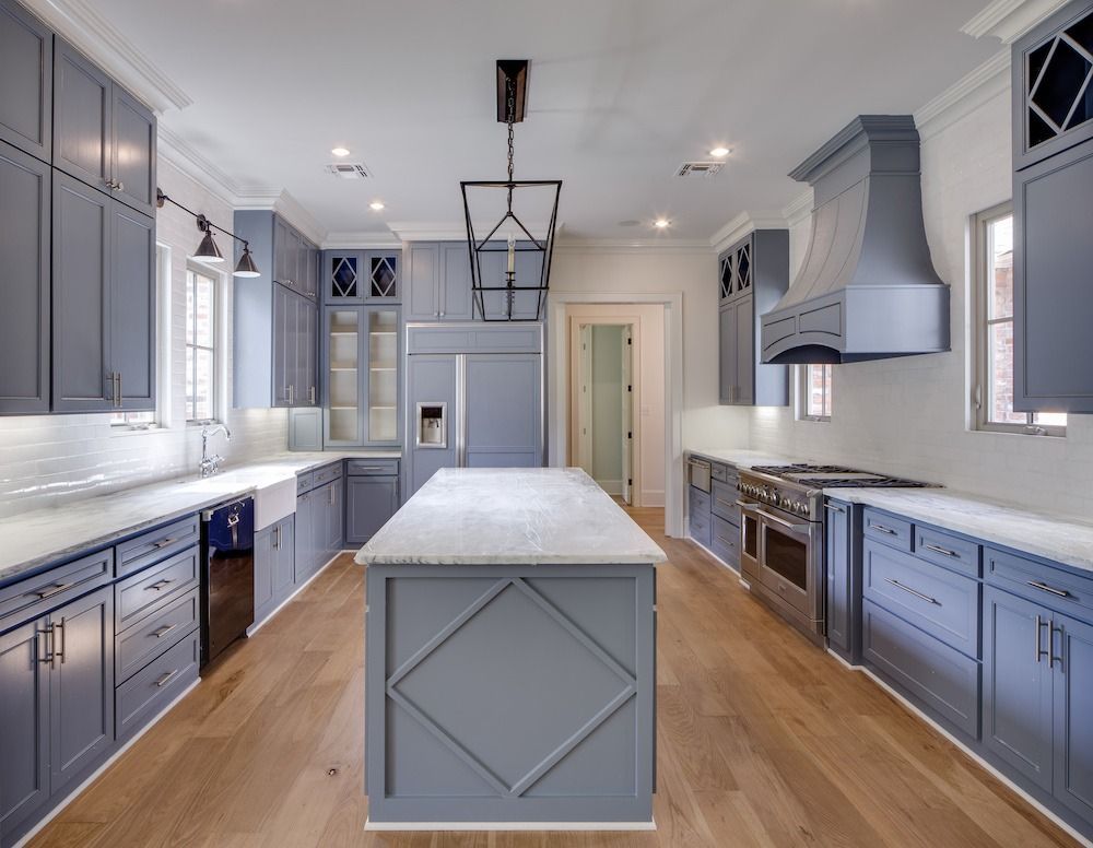 A modern kitchen features blue cabinets, a central island, stainless steel appliances, and wood floors.