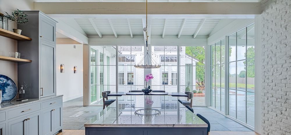 A bright, modern kitchen featuring a dark island, grey cabinetry, wood shelving, and large floor-to-ceiling glass windows.