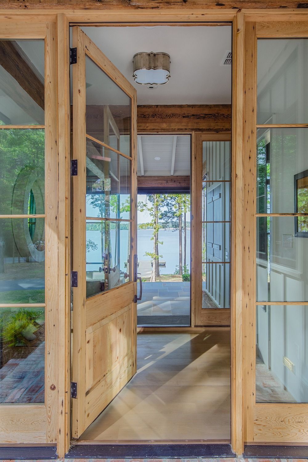 A rustic wooden-framed doorway opens to reveal a view of a lake through a bright, modern interior hallway.