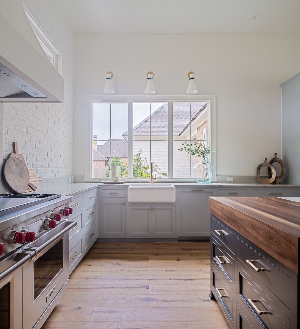 A kitchen with a stainless steel range, white brick backsplash, apron-front sink, light wood floors, and a dark island.