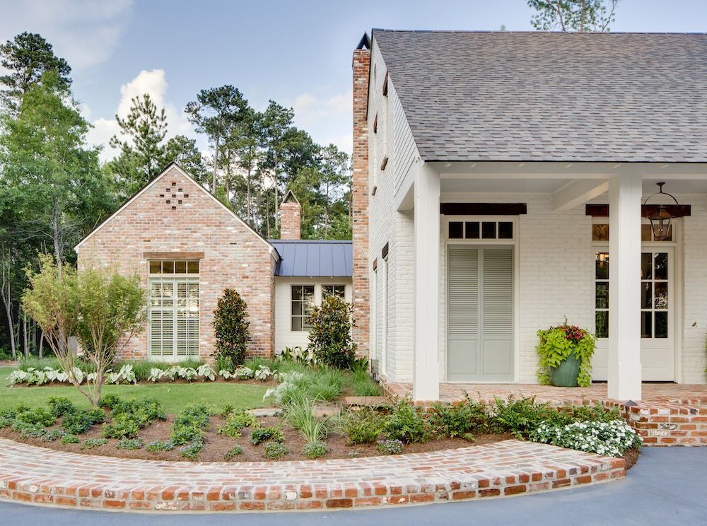 A white brick house with a gabled roof, arched window, and landscaped front yard with a curved brick garden wall.