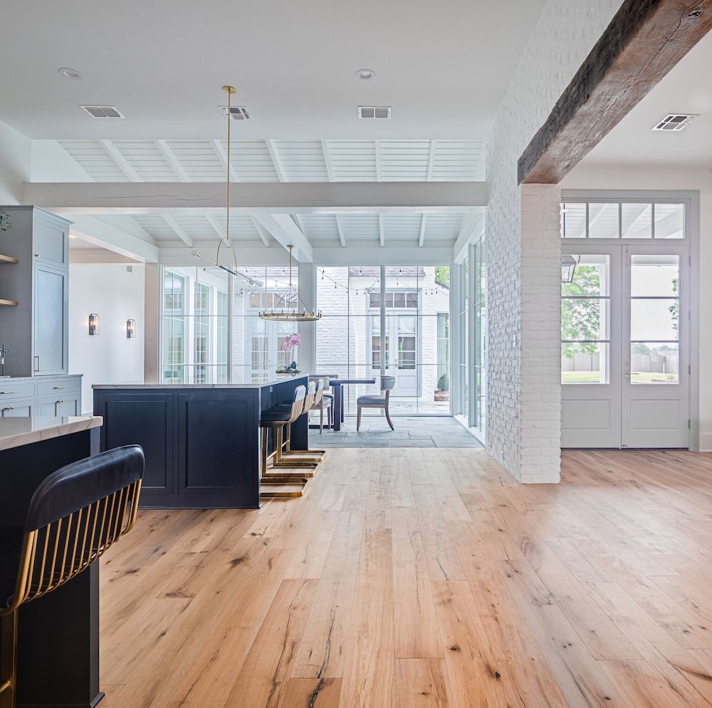 A bright, modern kitchen with light wood floors, a dark blue island, white brick details, and glass doors to a patio.