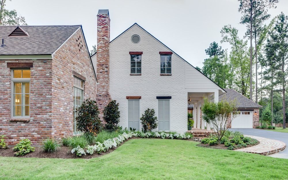 A two-story home with a brick exterior, white-painted facade, multiple windows, a prominent chimney, and a landscaped yard.