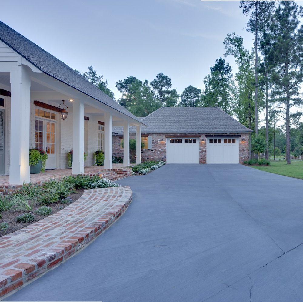 White house with a brick walkway and a side-facing two-car garage under a clear sky.