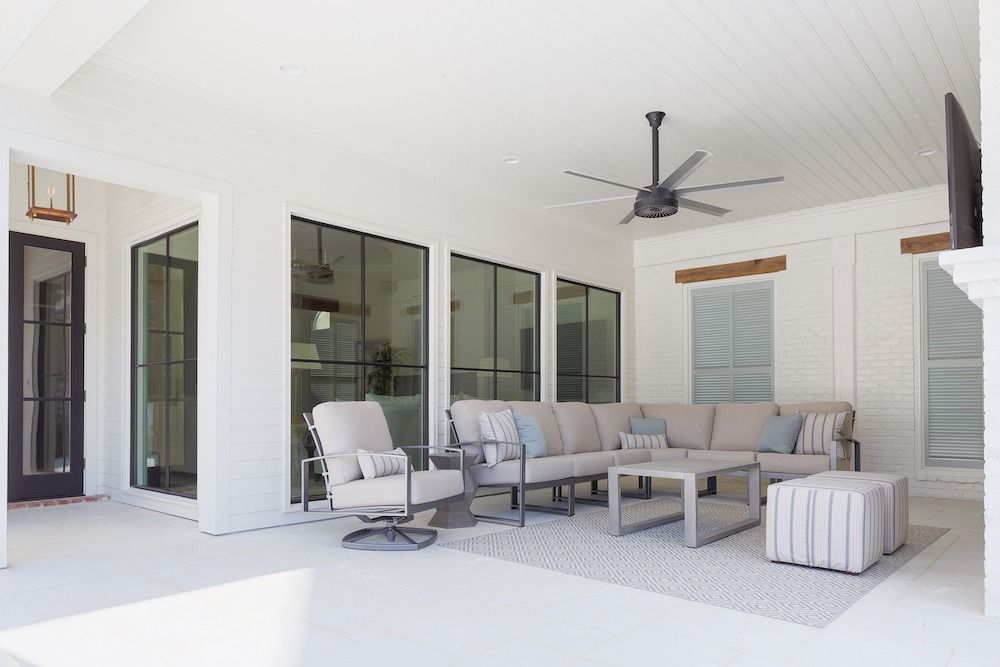 Modern outdoor patio with a beige sectional, an armchair, a coffee table, and an ottoman on a patterned rug under a fan.