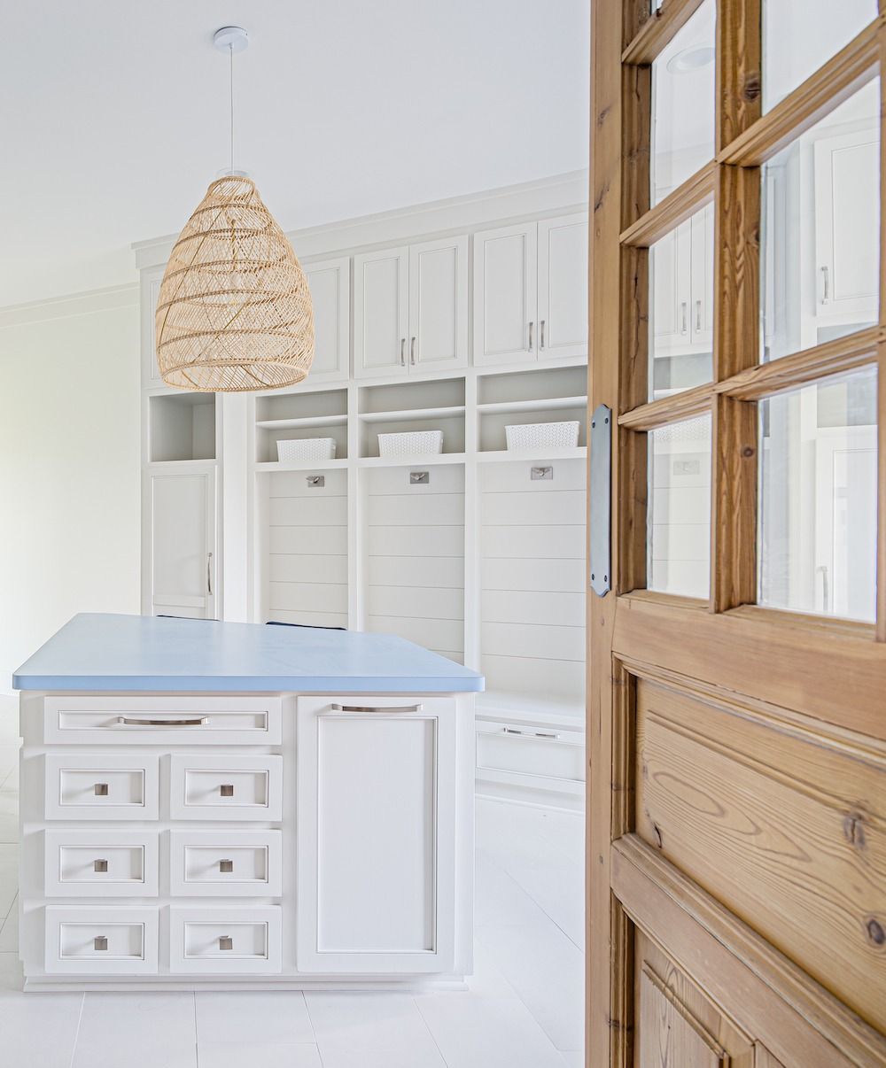 A wooden door opens into a room with white built-in cabinetry, an island with a blue top, and a textured pendant light.