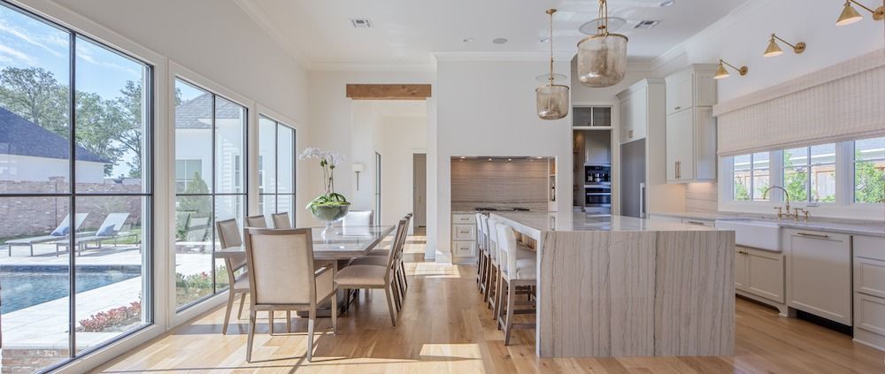 A bright, modern kitchen and dining area with light wood floors, a white kitchen island, and large floor-to-ceiling windows.