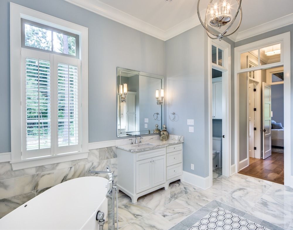 A bright, modern bathroom with a white freestanding tub, marble floors, a vanity with a mirror, and light blue walls.