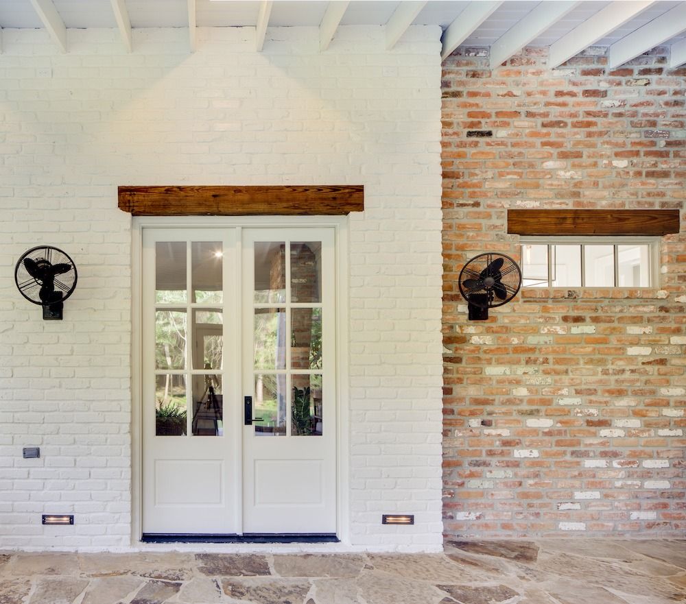 A patio with a white double door and a raw brick wall, featuring exposed wooden beams and black wall-mounted fans.