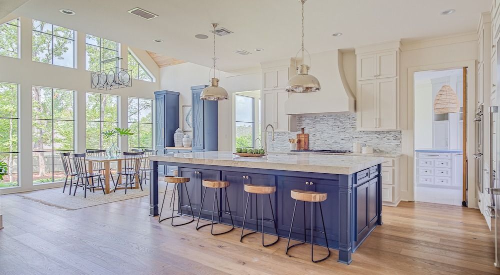 Modern kitchen with a large navy blue island, bar stools, white cabinetry, marble backsplash, and a dining area.