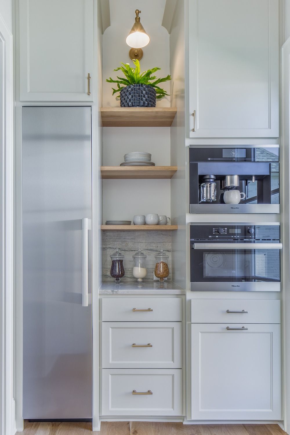 A kitchen pantry wall with a stainless steel refrigerator, white cabinetry, open wooden shelves, and built-in appliances.