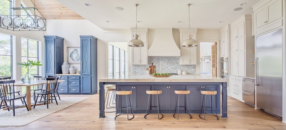 A bright, modern kitchen features blue cabinets and a central island with four bar stools, wood floors, and pendant lights.