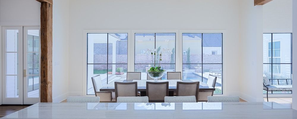 A bright dining room with a table, six chairs, and large windows overlooking a patio and pool.