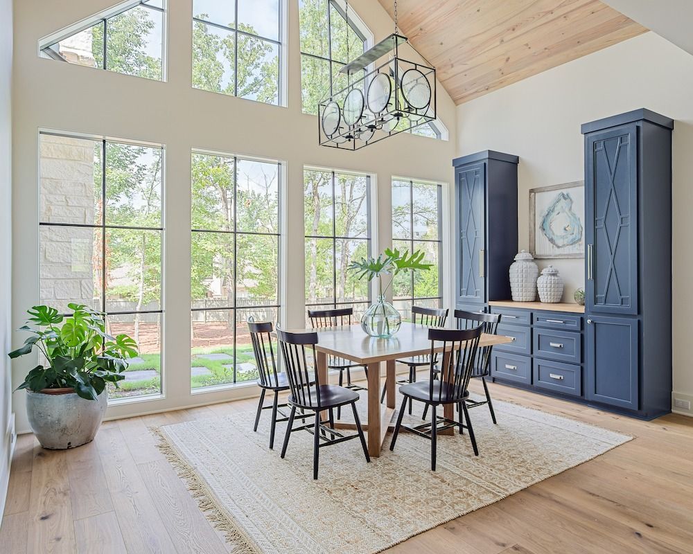 Dining room with light wood floors, a wooden table and chairs on a woven rug, beneath a black lantern-style chandelier.