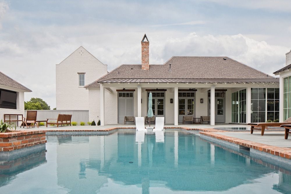 A backyard swimming pool with two lounge chairs in the water, facing a white house with a tall brick chimney.