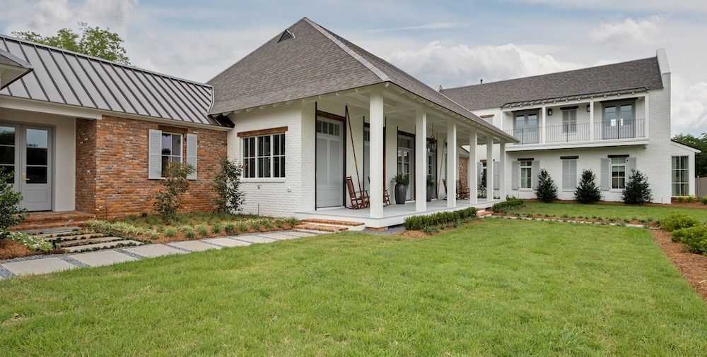 A large white house with a brick section, a covered porch, and a grassy lawn under a cloudy sky.
