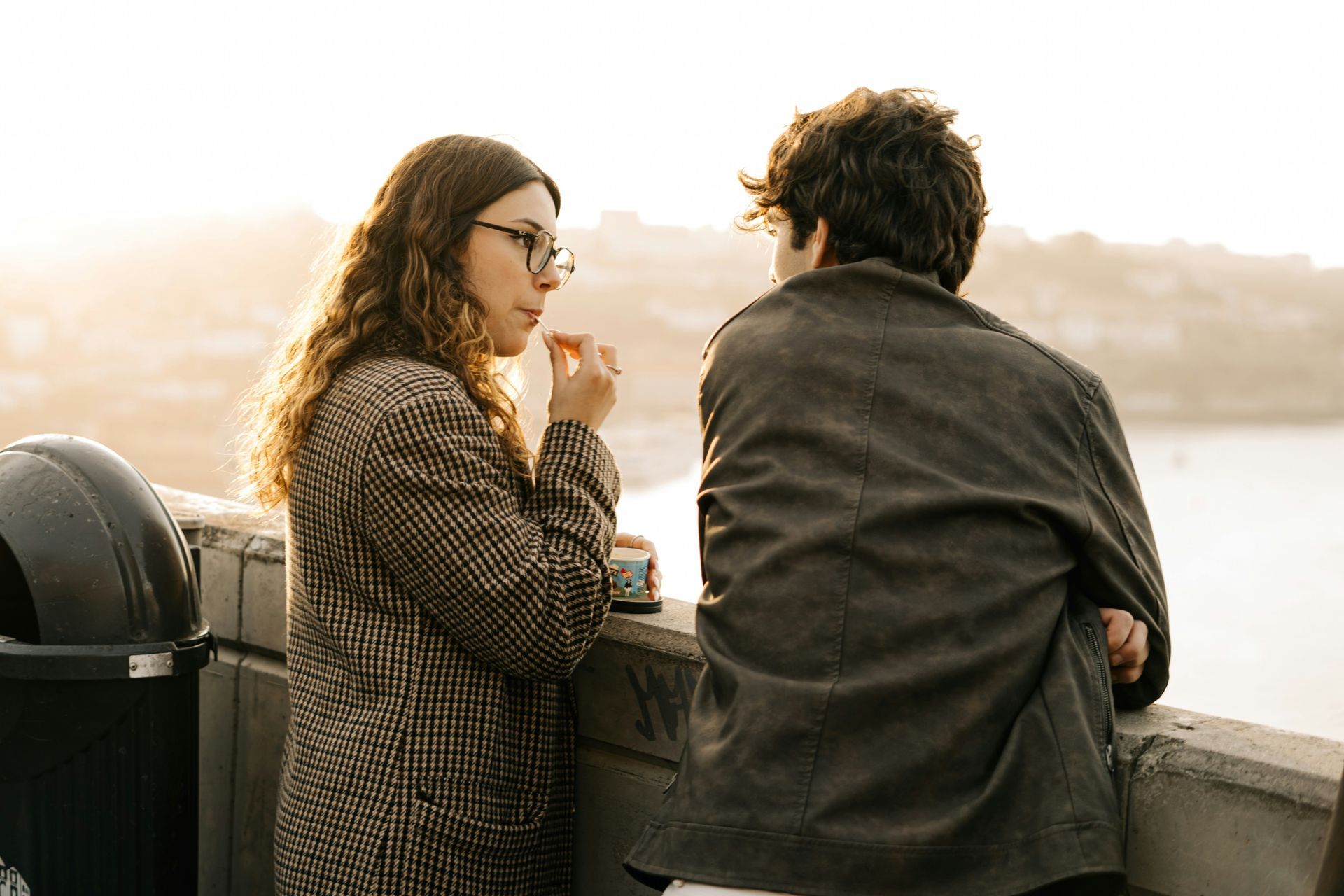 A man is sitting at a desk using a laptop and talking on a cell phone.