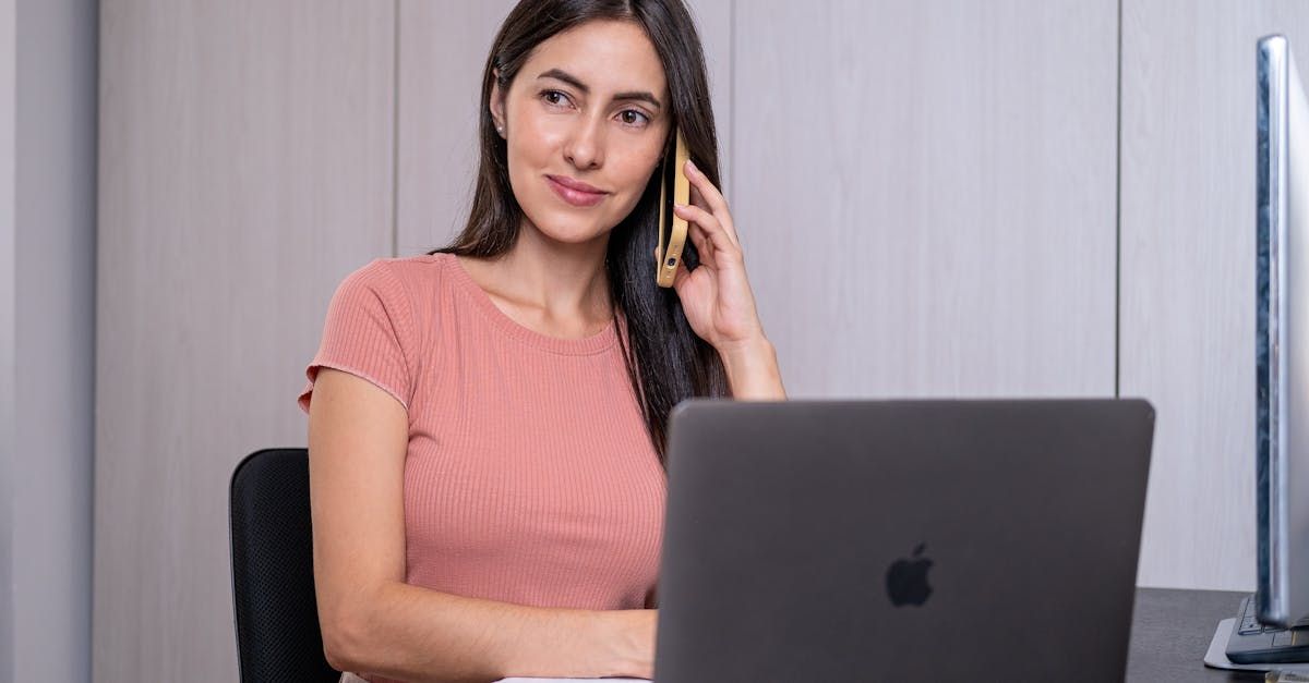 A woman is sitting in front of a laptop computer talking on a cell phone.