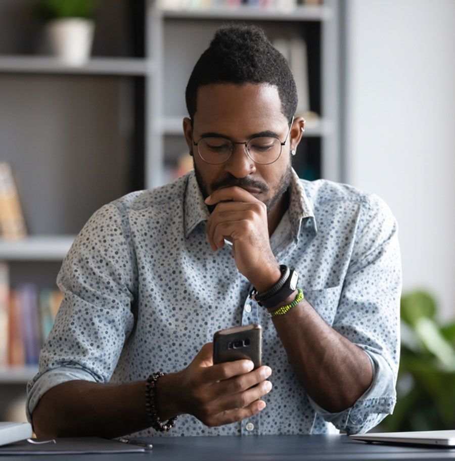 A man is sitting at a desk looking at his cell phone