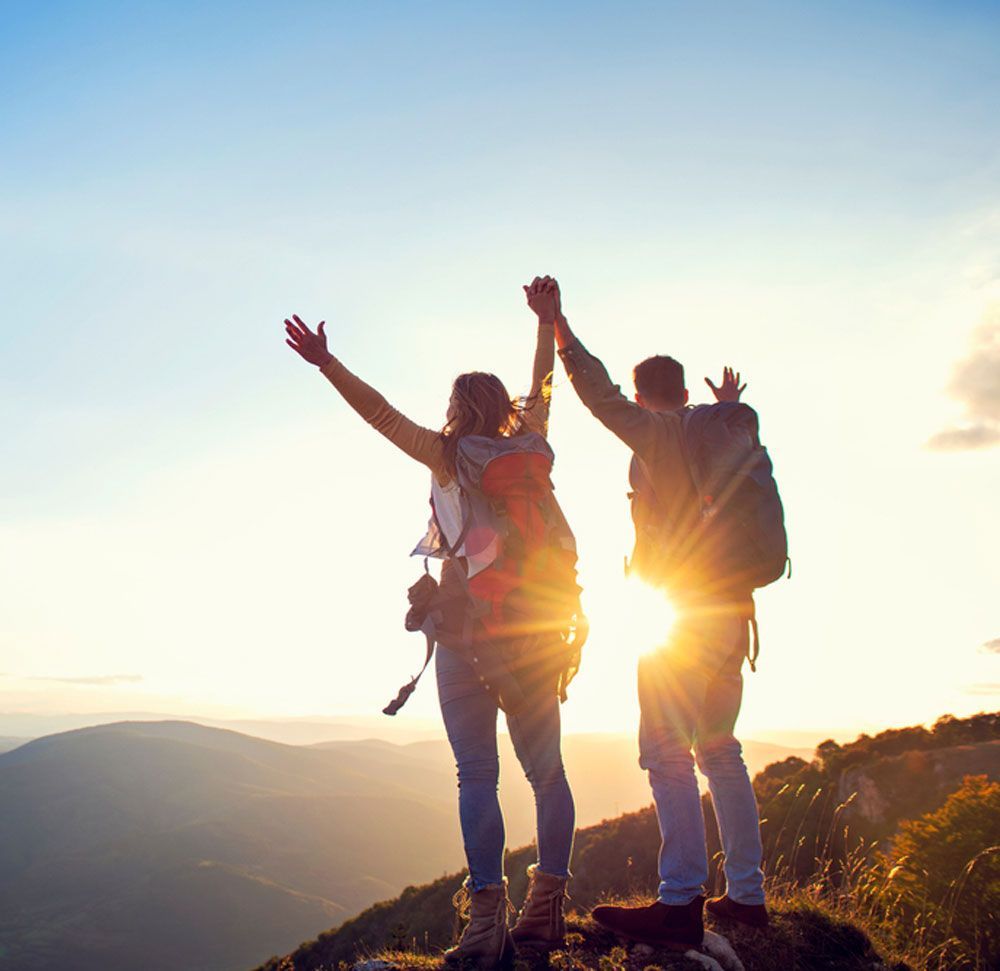 A man and a woman are standing on top of a mountain with their arms in the air.