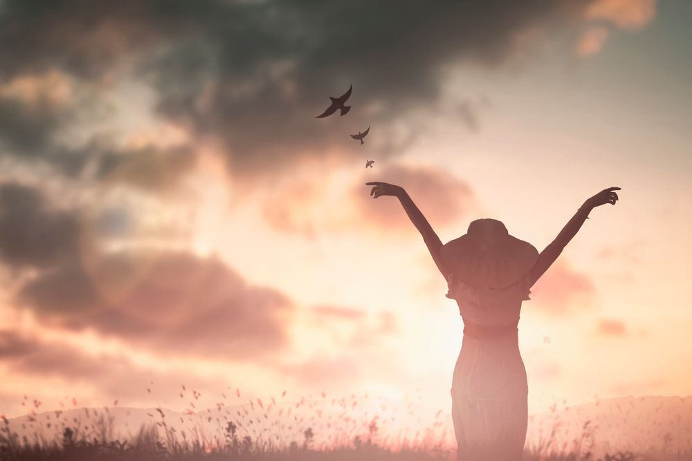 A woman is standing in a field with her arms outstretched at sunset.