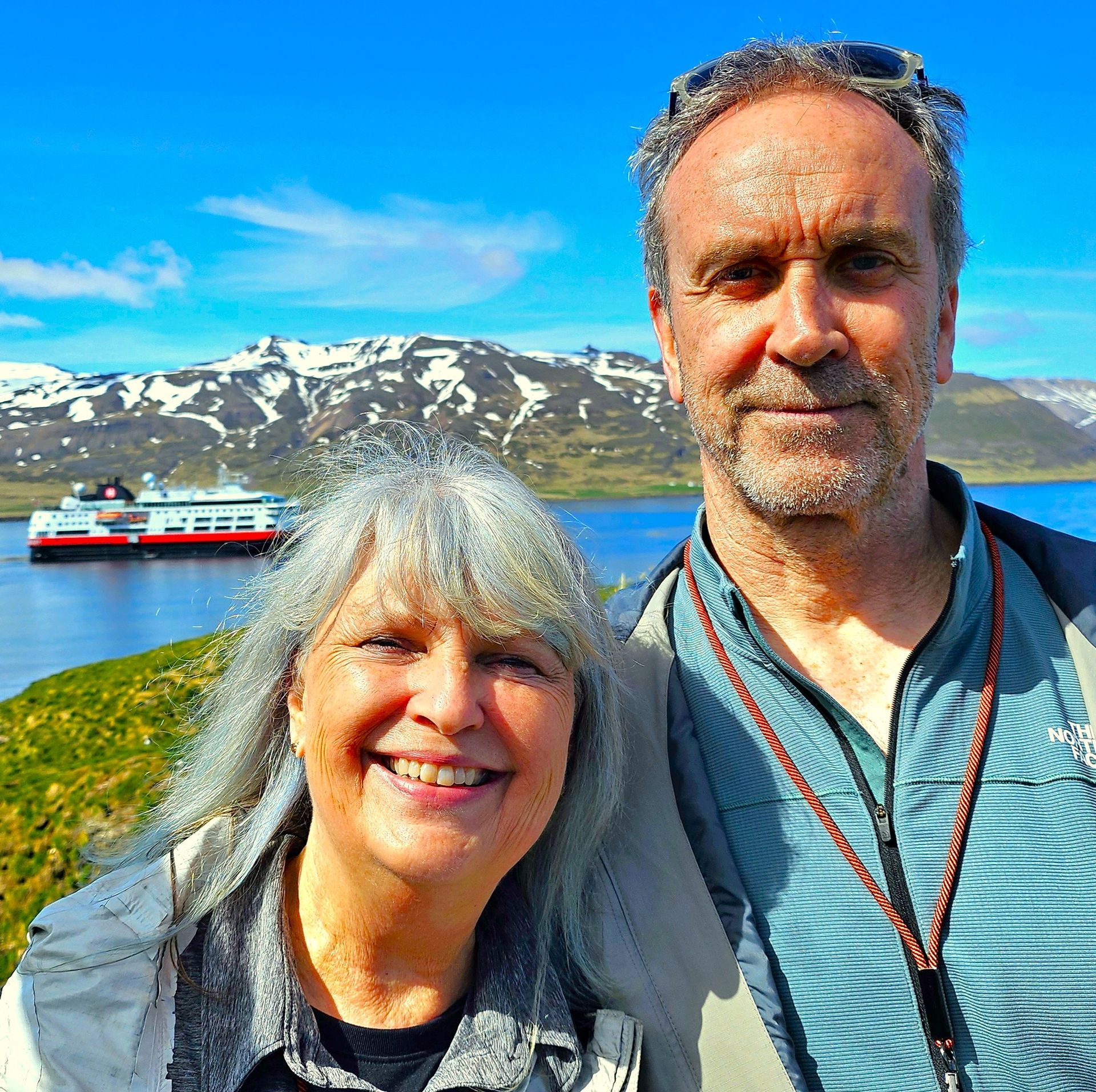 A man and a woman are posing for a picture with a boat in the background.