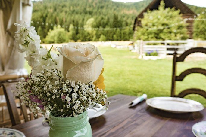 A table with flowers and plates on it with a rustic farm background.