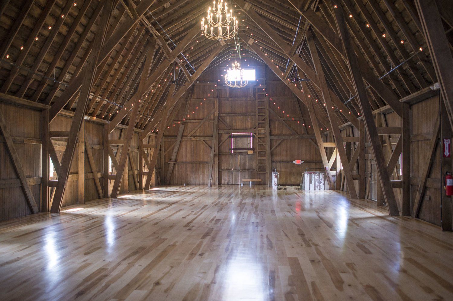 A large empty barn with a wooden floor and a chandelier hanging from the ceiling.