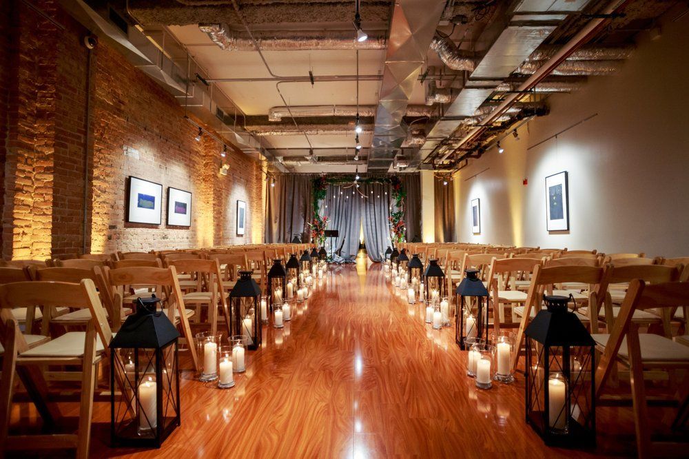 A long room set up for a wedding ceremony with lanterns.