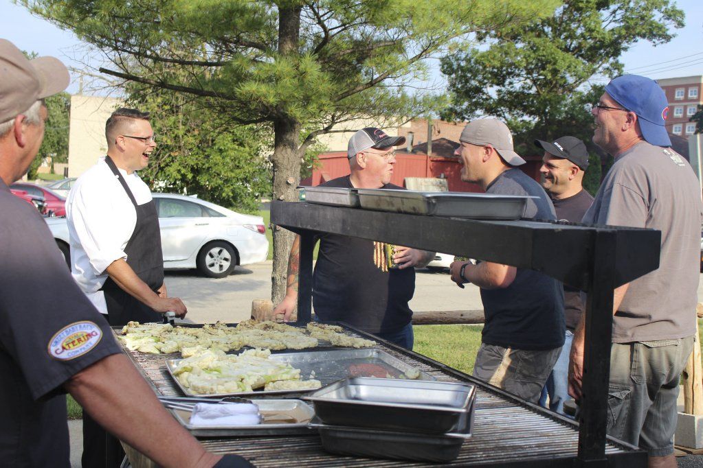 A group of men are standing around a table with food on it.