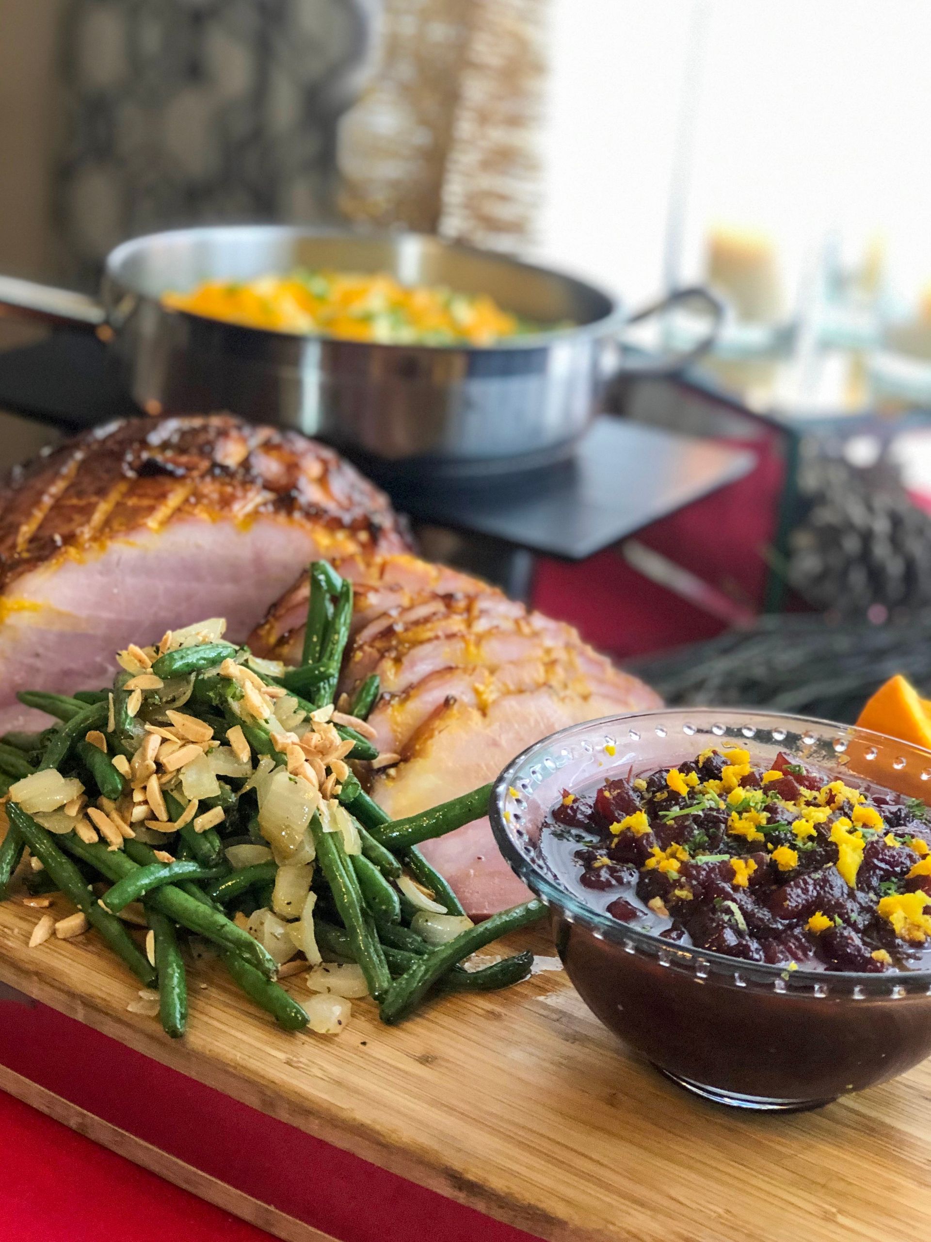 ham and green beans with a bowl of cranberry sauce on a wood board